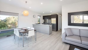 Une cuisine moderne dotée d’un îlot central, un coin repas avec une table et des chaises, un canapé gris et une grande fenêtre offrant une vue sur l’extérieur.