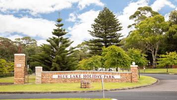 Un letrero de piedra con la inscripción "Blue Lake Holiday Park" rodeado de exuberante follaje y árboles.