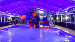Un toboggan aquatique intérieur doté d’un toit transparent et d’un espace piscine.