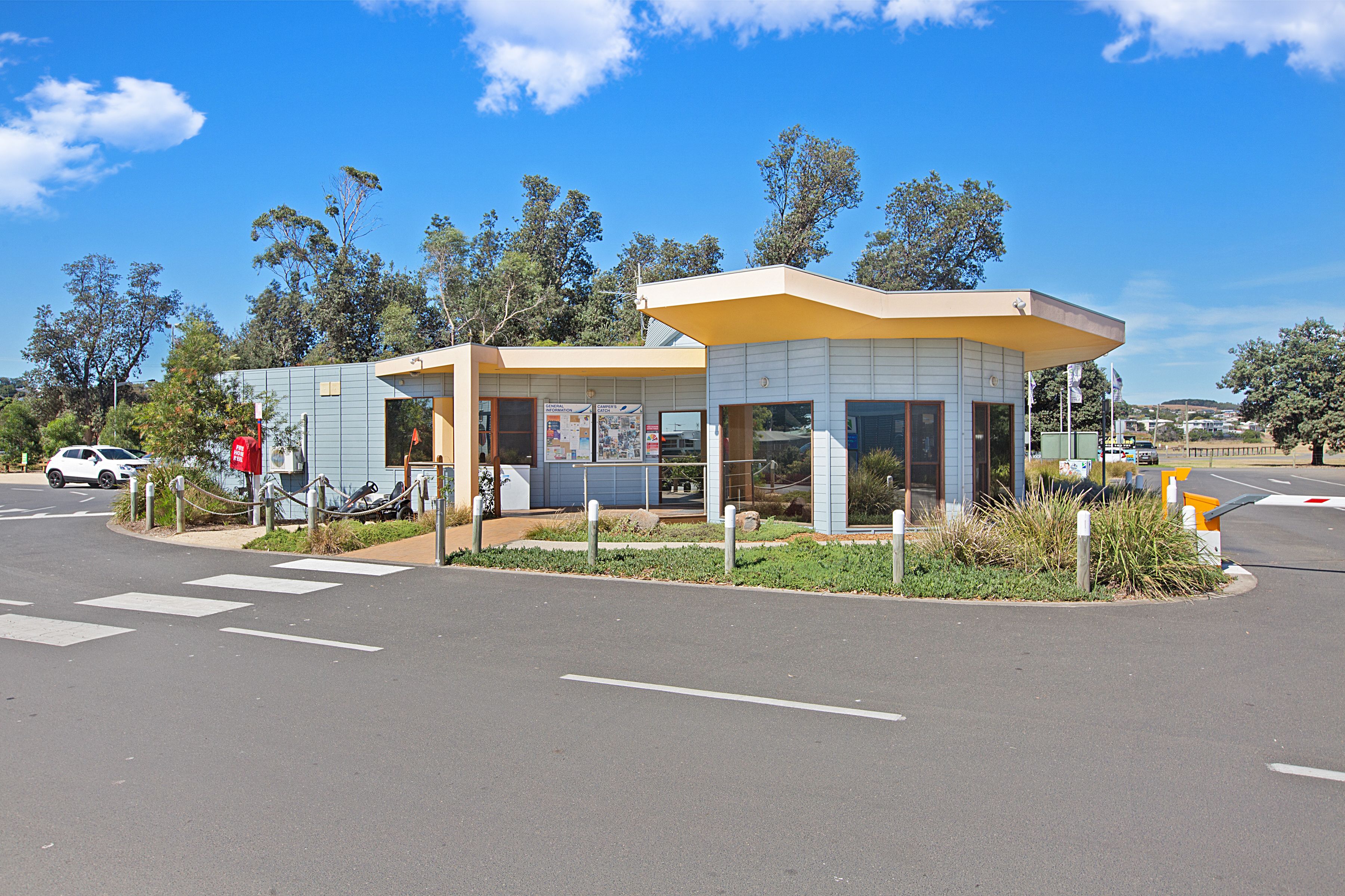 A small, modern building with a flat roof and large windows, located at a street corner with a pedestrian crossing.