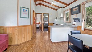 A room with wooden floors, a white table with chairs, a kitchenette, and a bed in the background. - Bellarine Bayside Holiday Parks (Portarlington)