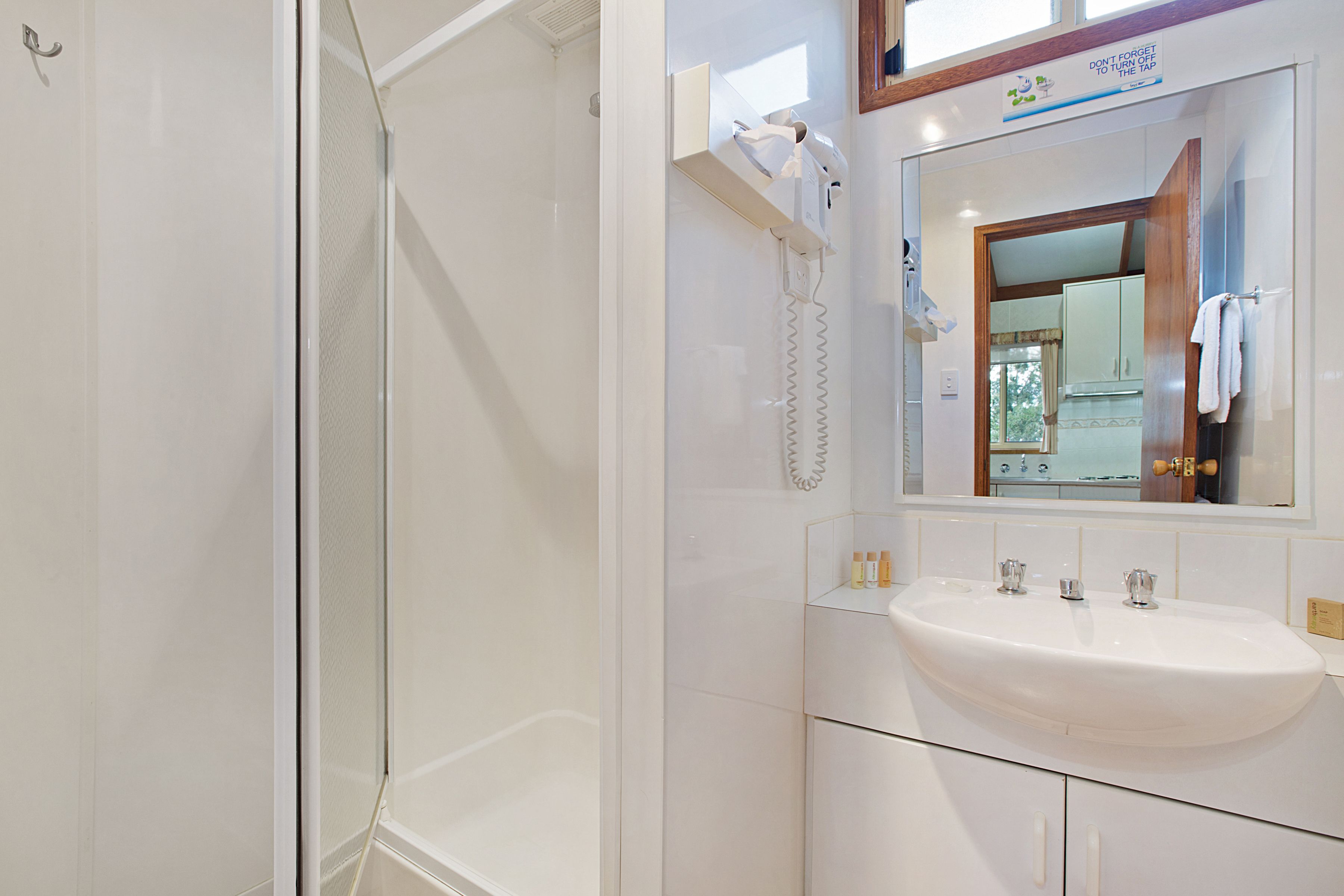 Un baño moderno con ducha envuelta en vidrio, un lavabo blanco con un espejo encima y un perchero con una toalla colgando.