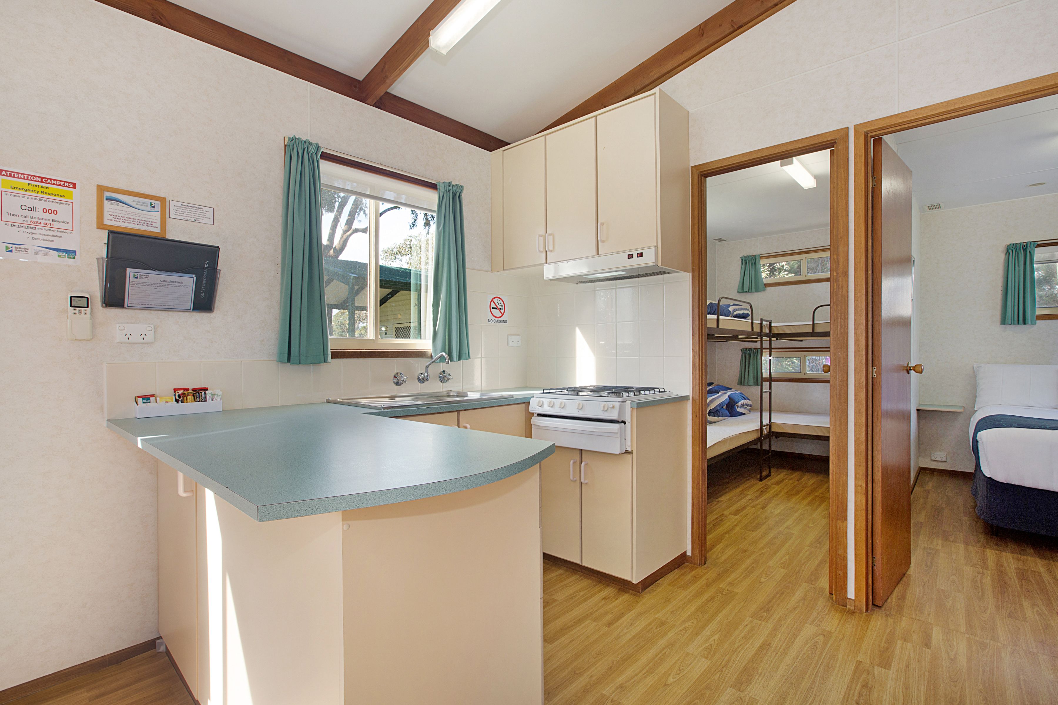 Cocina compacta con estufa, fregadero y armarios. Hay una cama litera en la habitación contigua.