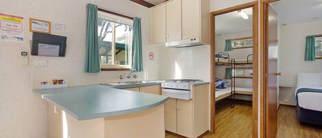 Cocina compacta con estufa, fregadero y armarios. Hay una cama litera en la habitación contigua.