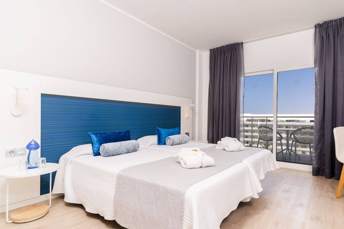 A modern hotel room with a large bed, a desk, and a balcony with a view of the city.