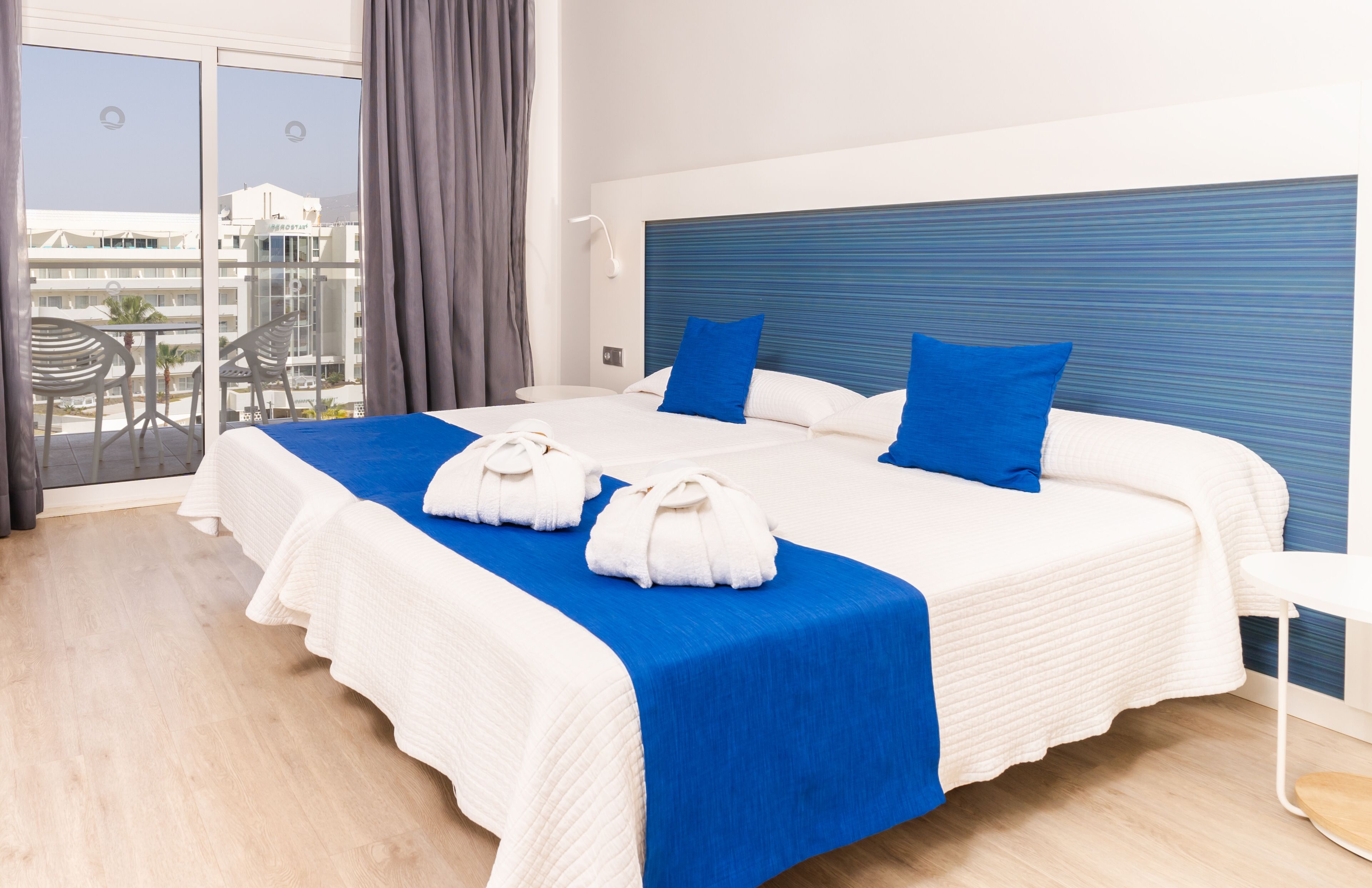 Une chambre d’hôtel avec un grand lit, une vue sur la ville et un balcon équipé de chaises.