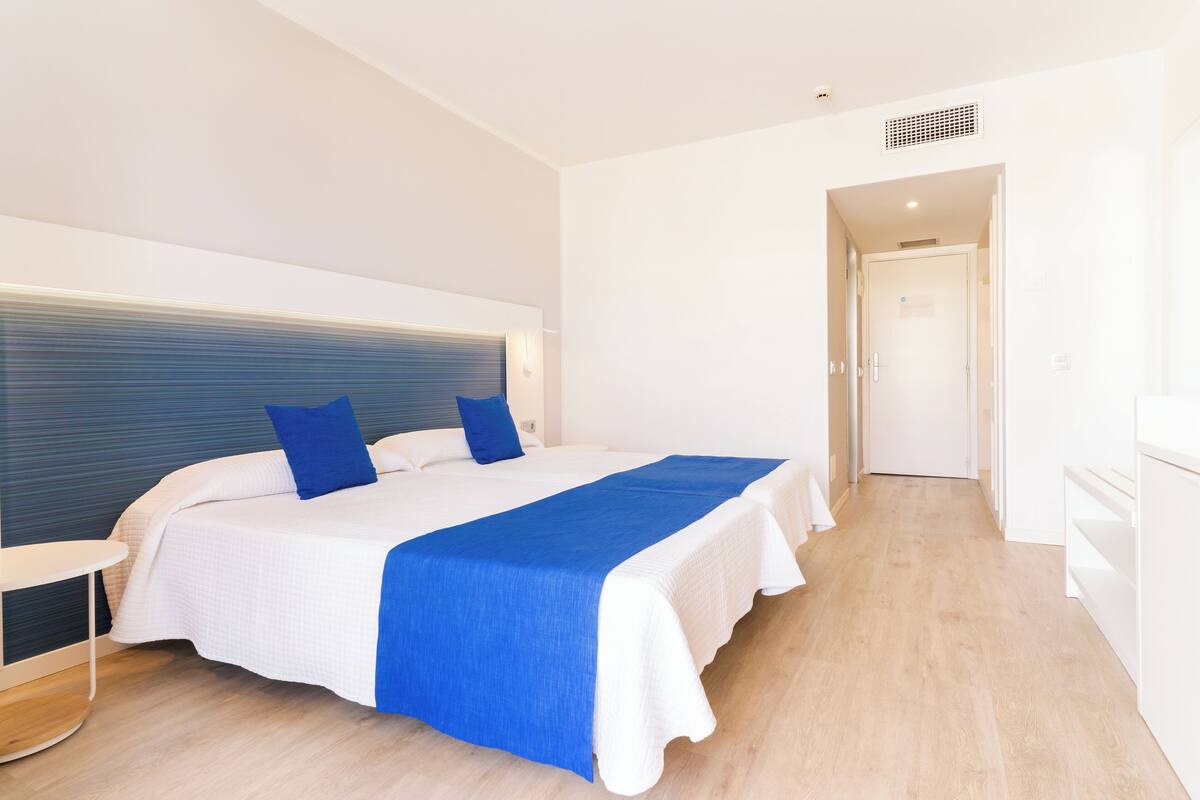 A hotel room with a large bed, two pillows, a bedside table, and a nightstand.
