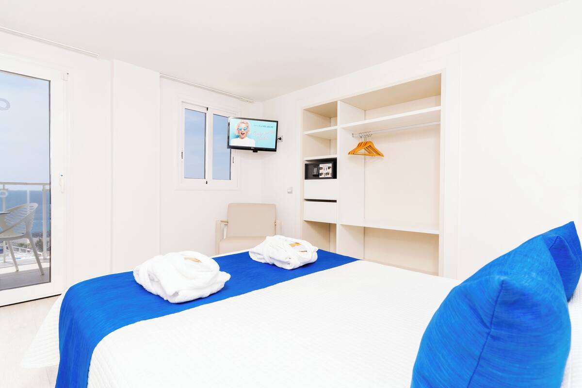 A hotel room with a bed, a TV, a chair, a wardrobe, and a balcony.