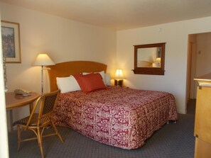 A hotel room with a bed, two bedside lamps, a chair, a desk with a phone, a mirror, and a framed picture on the wall. - Colusa Riverside Inn (Colusa)