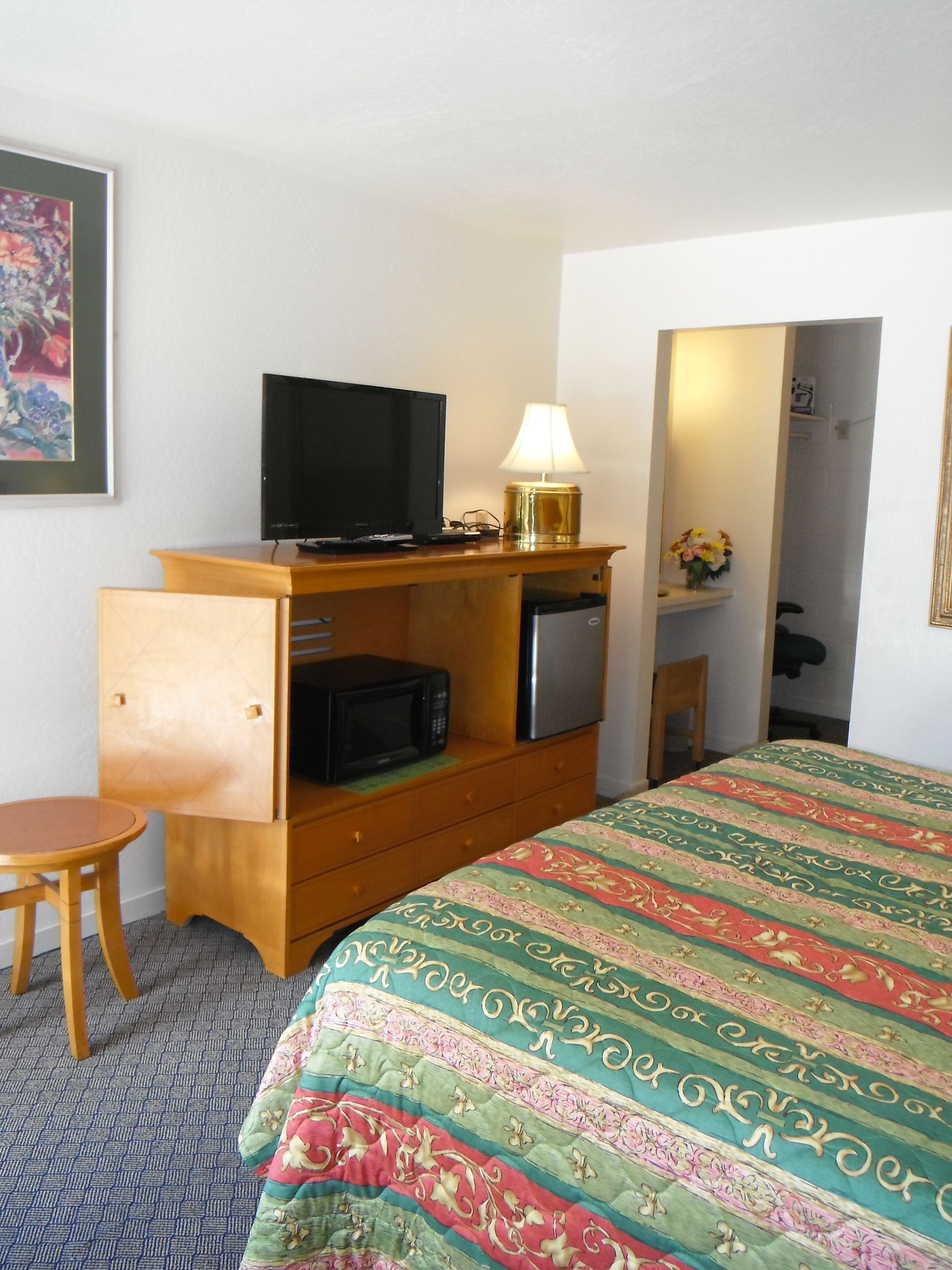 Ein Hotelzimmer mit einem Bett, einem Schreibtisch mit Fernseher, einer Mikrowelle, einem Kühlschrank, einer Lampe und einem Sessel.
