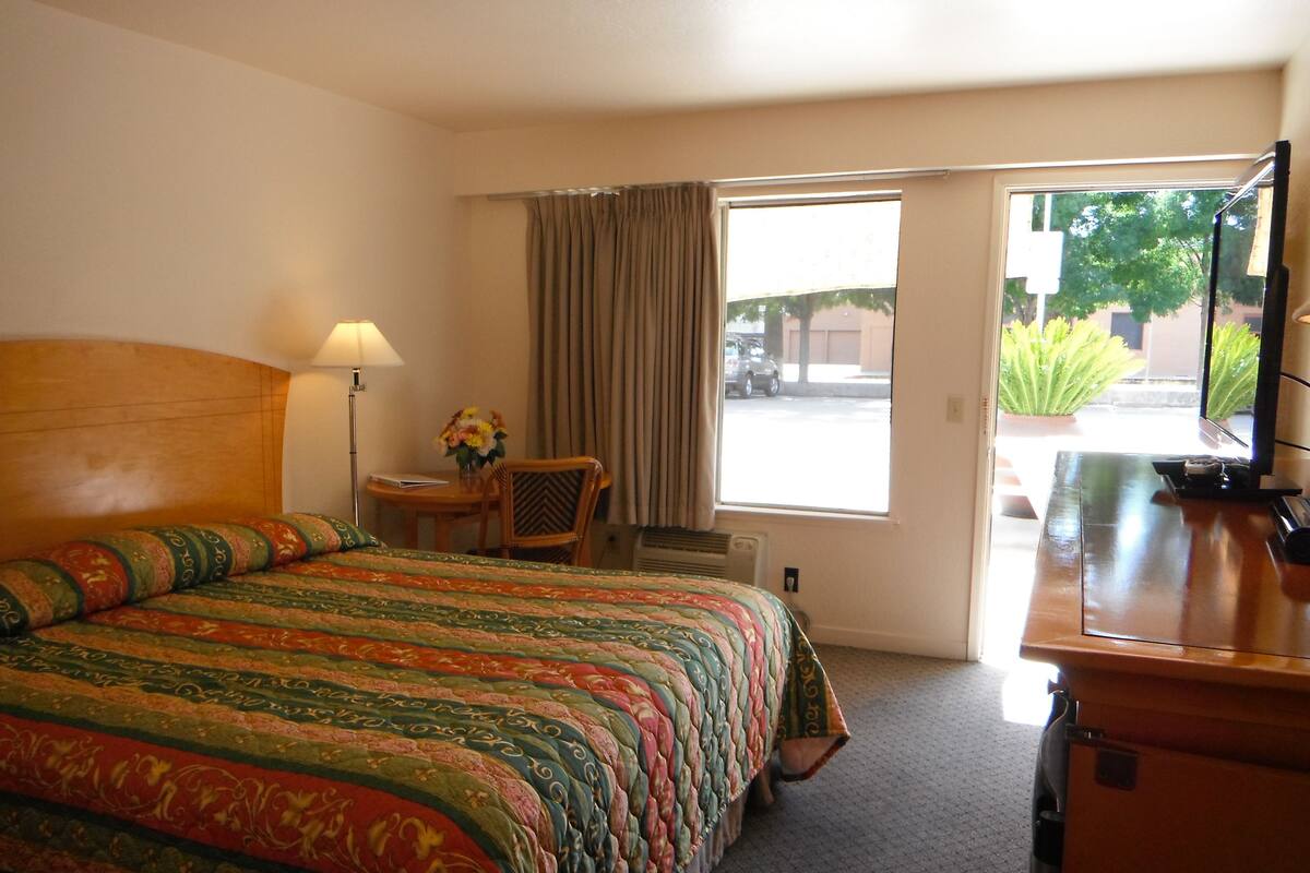 A hotel room with a large bed, a desk, a chair, a lamp, and a television.