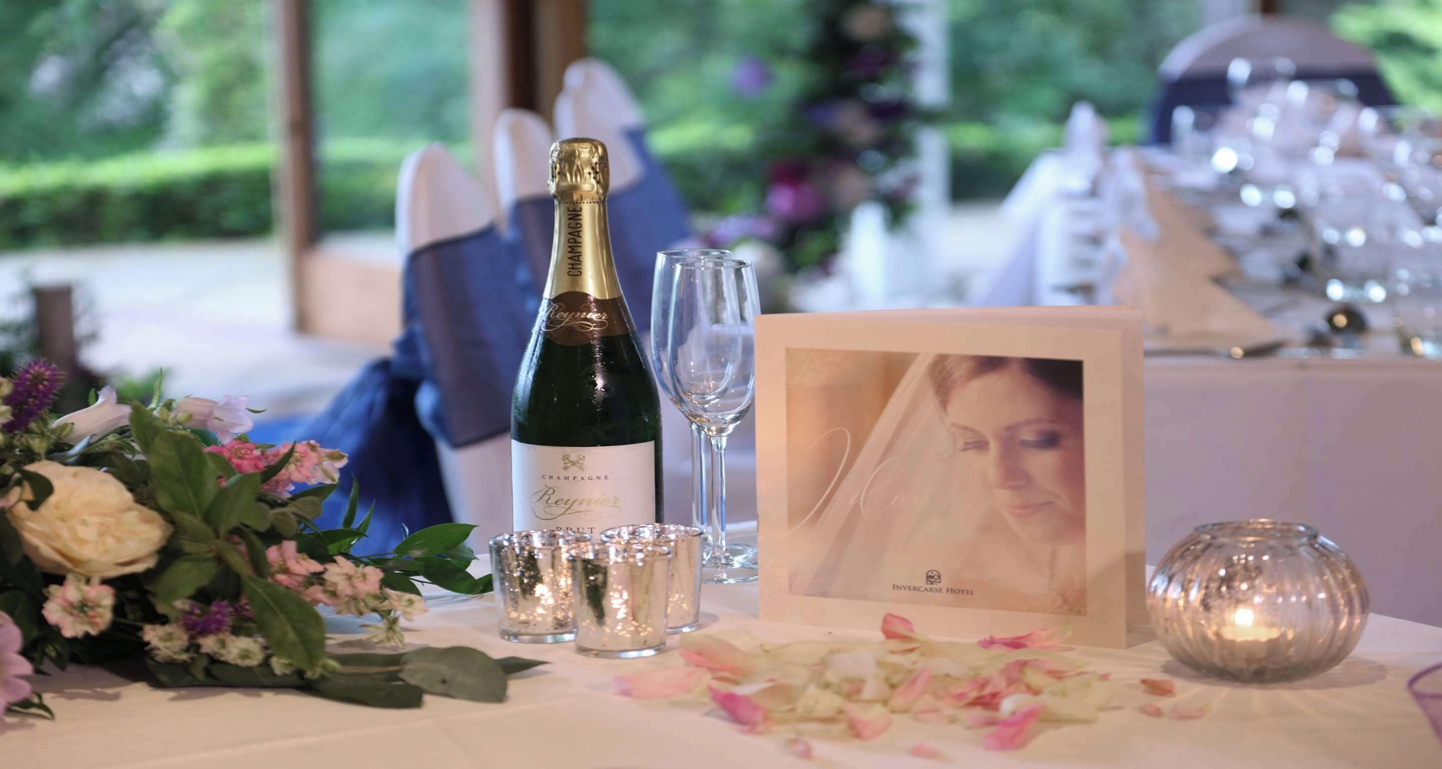 A table set with a bottle of champagne, shot glasses, a framed photo, and a candle.