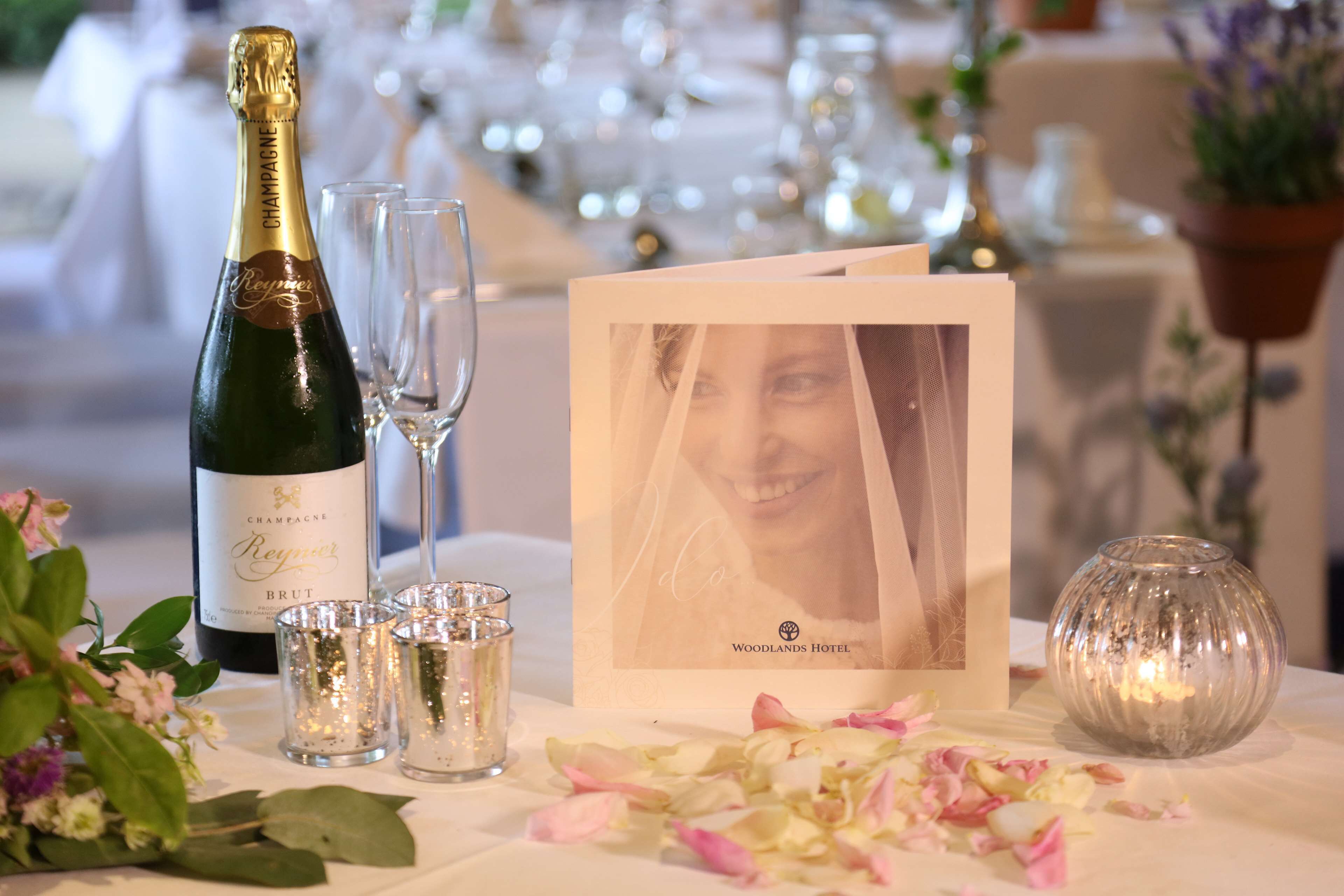 A table setting with a bottle of champagne, glasses, a framed photo, and a candle.