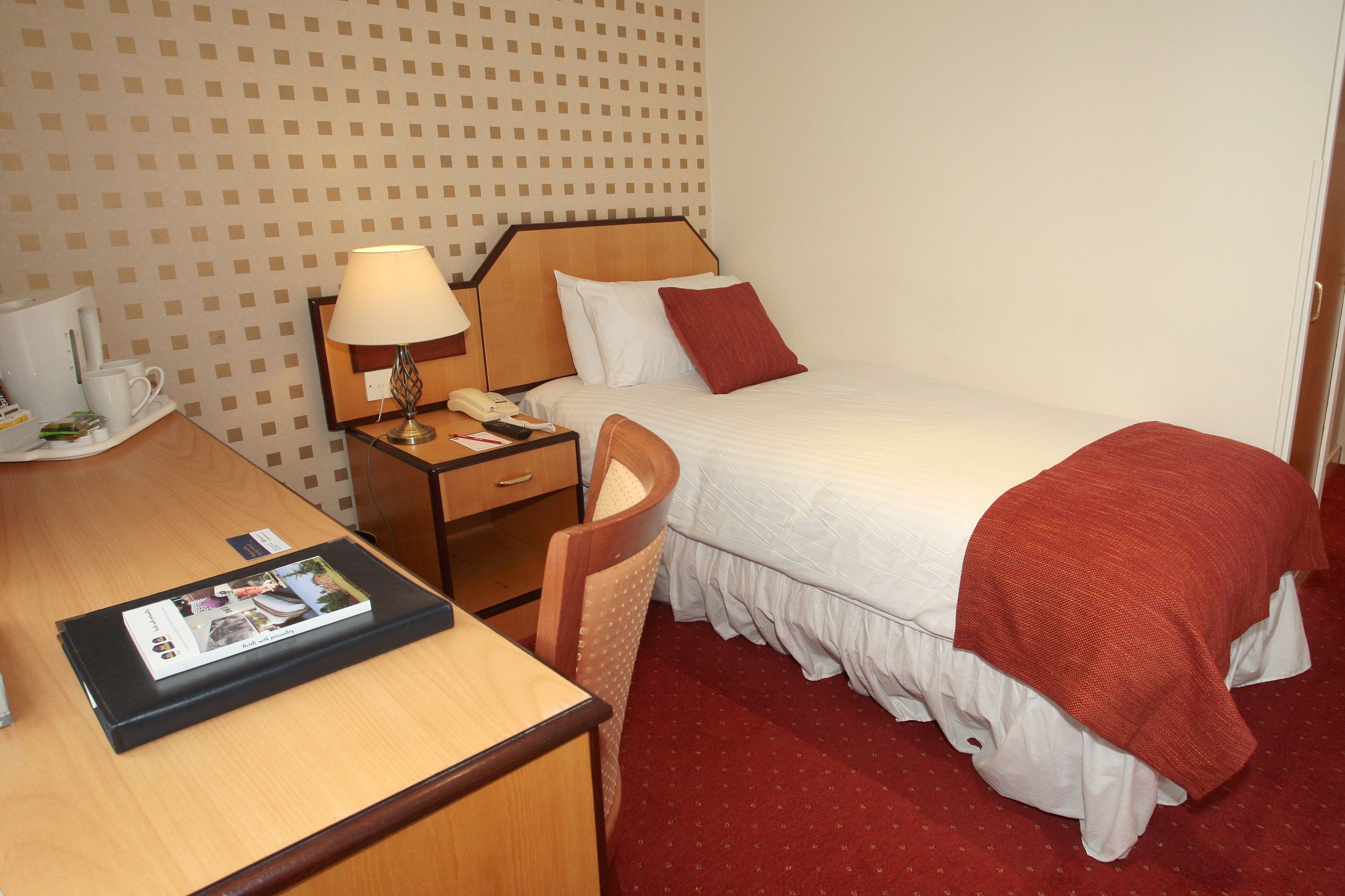 Ein Hotelzimmer mit Bett, Schreibtisch, Stuhl, Nachttisch und Lampe.