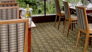 A dining area with a view of a lake, wooden chairs, a table set with glasses, and a bottle of wine.