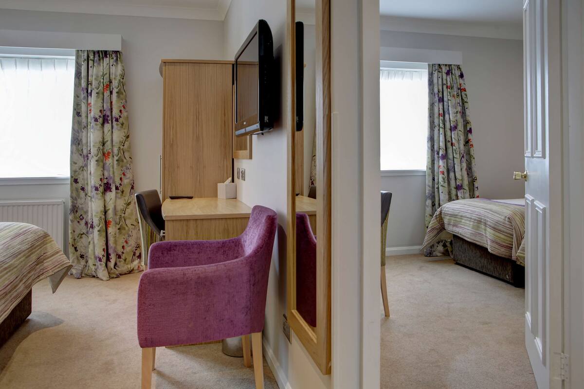 A bedroom with a bed, a desk, a chair, a wardrobe, and a television.