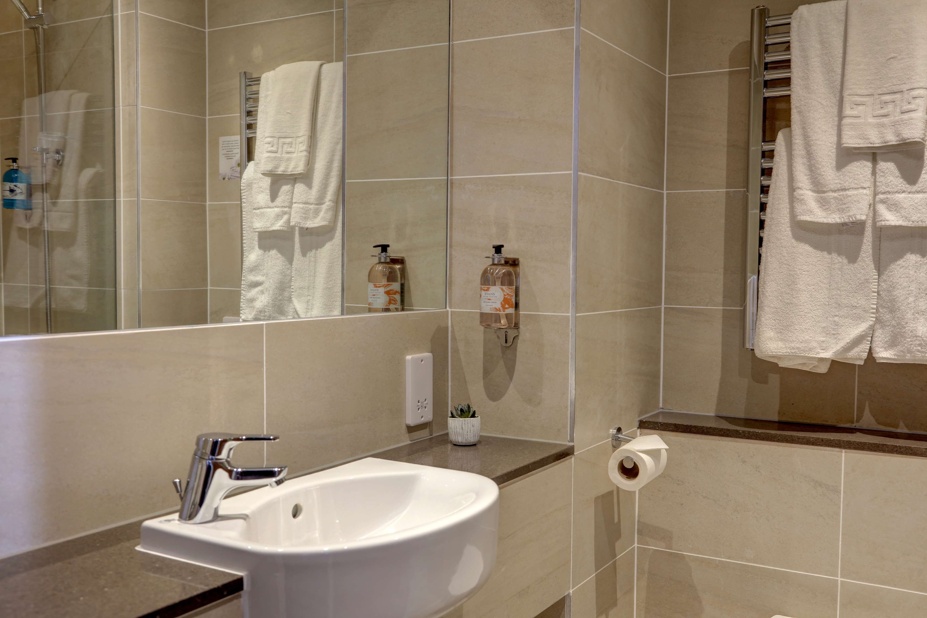 A modern bathroom with a white sink, mirror, and beige tiles.