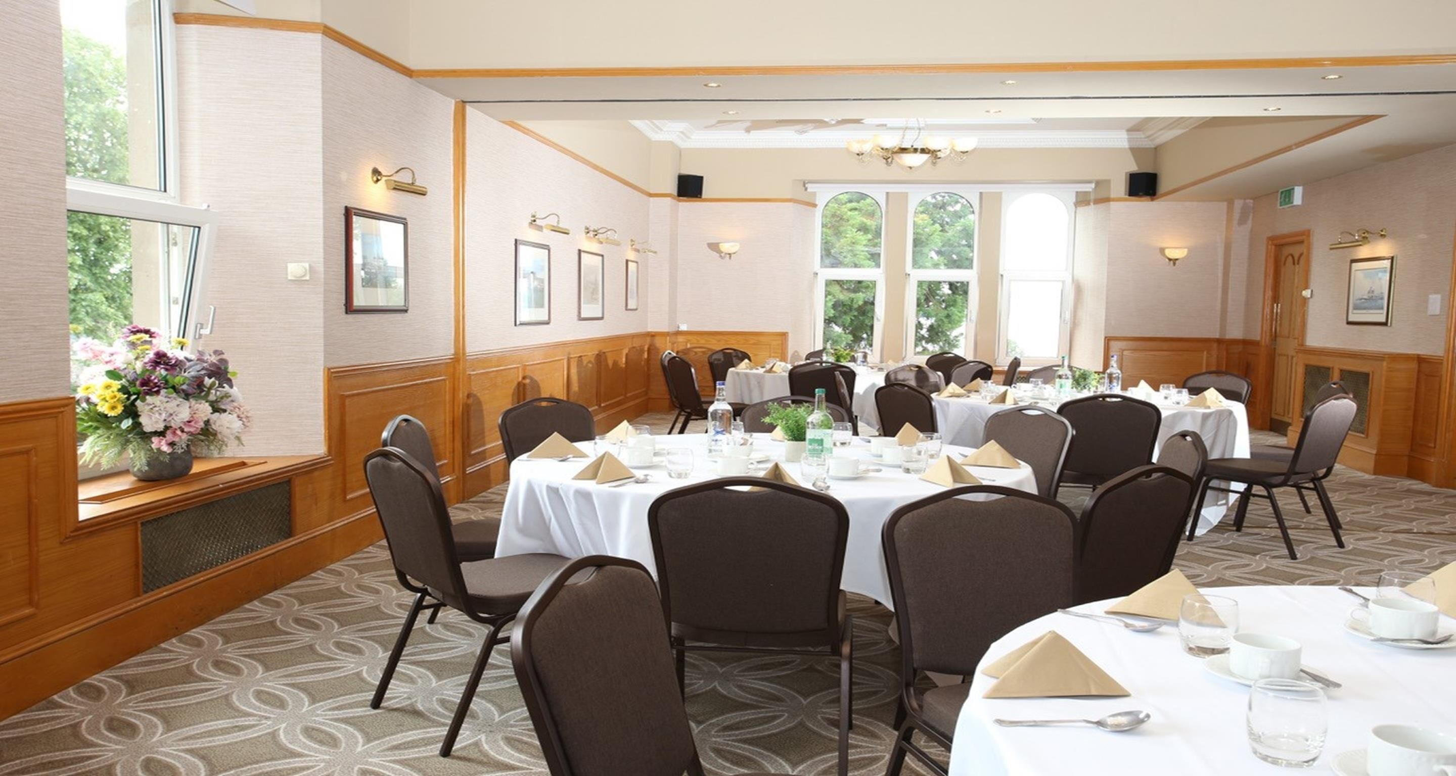 A conference room with multiple round tables, chairs, and a large window with a view of trees.