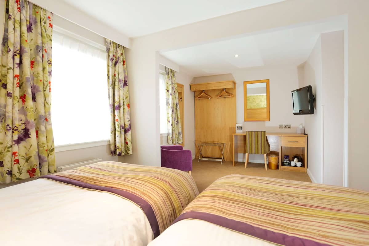 A hotel room with two beds, a desk, a chair, a television, and a wardrobe.