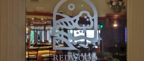 Se ve a través de una ventana un letrero de restaurante con un logotipo y el nombre 'REDWOOD RESTAURANT'.