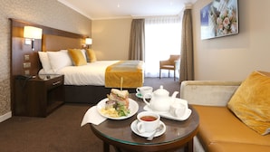 A hotel room with a bed, a sitting area, and a dining table with breakfast items.