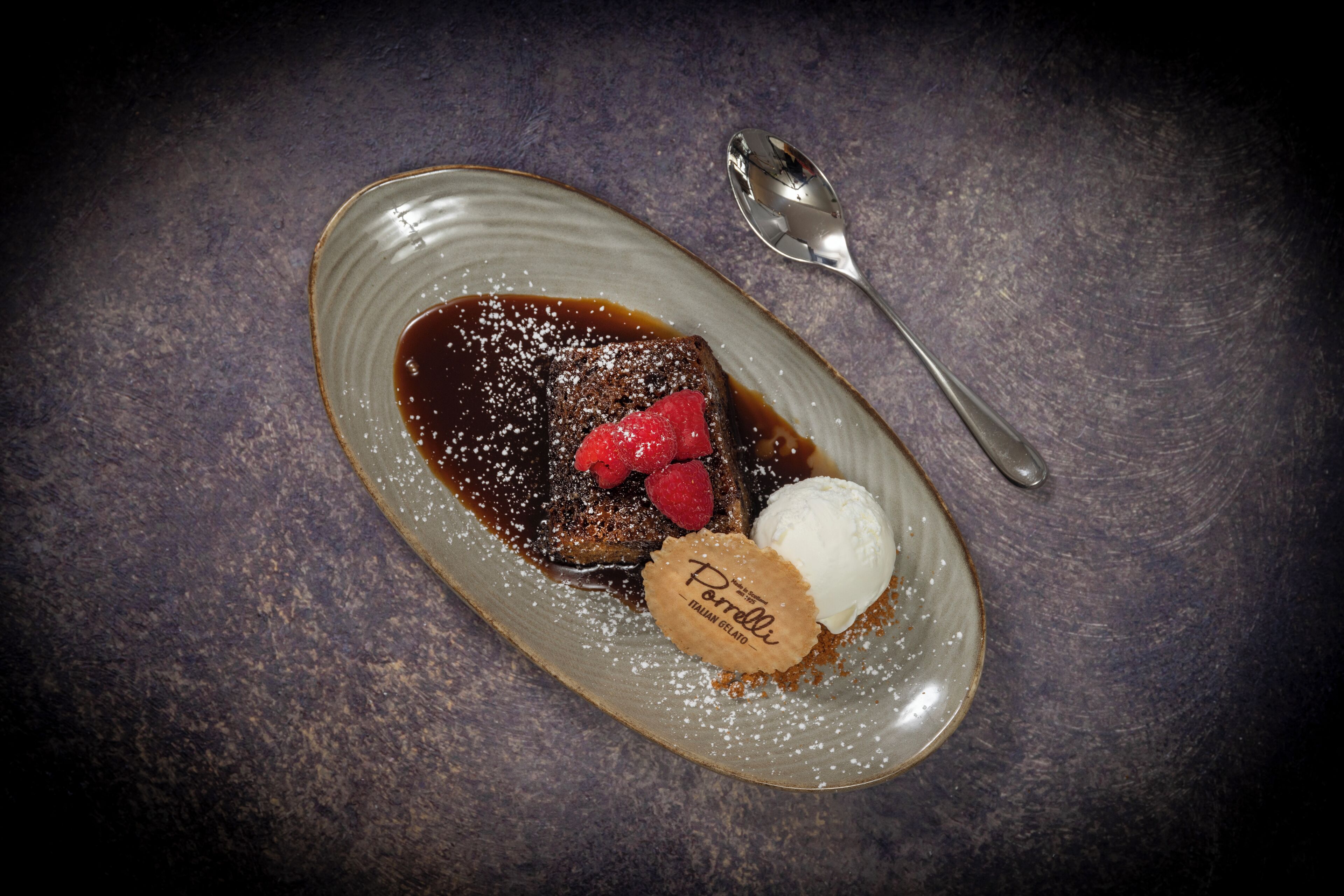 A dessert plate with a chocolate dessert, raspberries, and a scoop of ice cream on a textured surface.