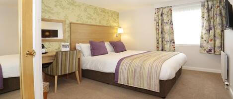 A hotel room with a bed, a desk, a chair, a TV, and a window with curtains.