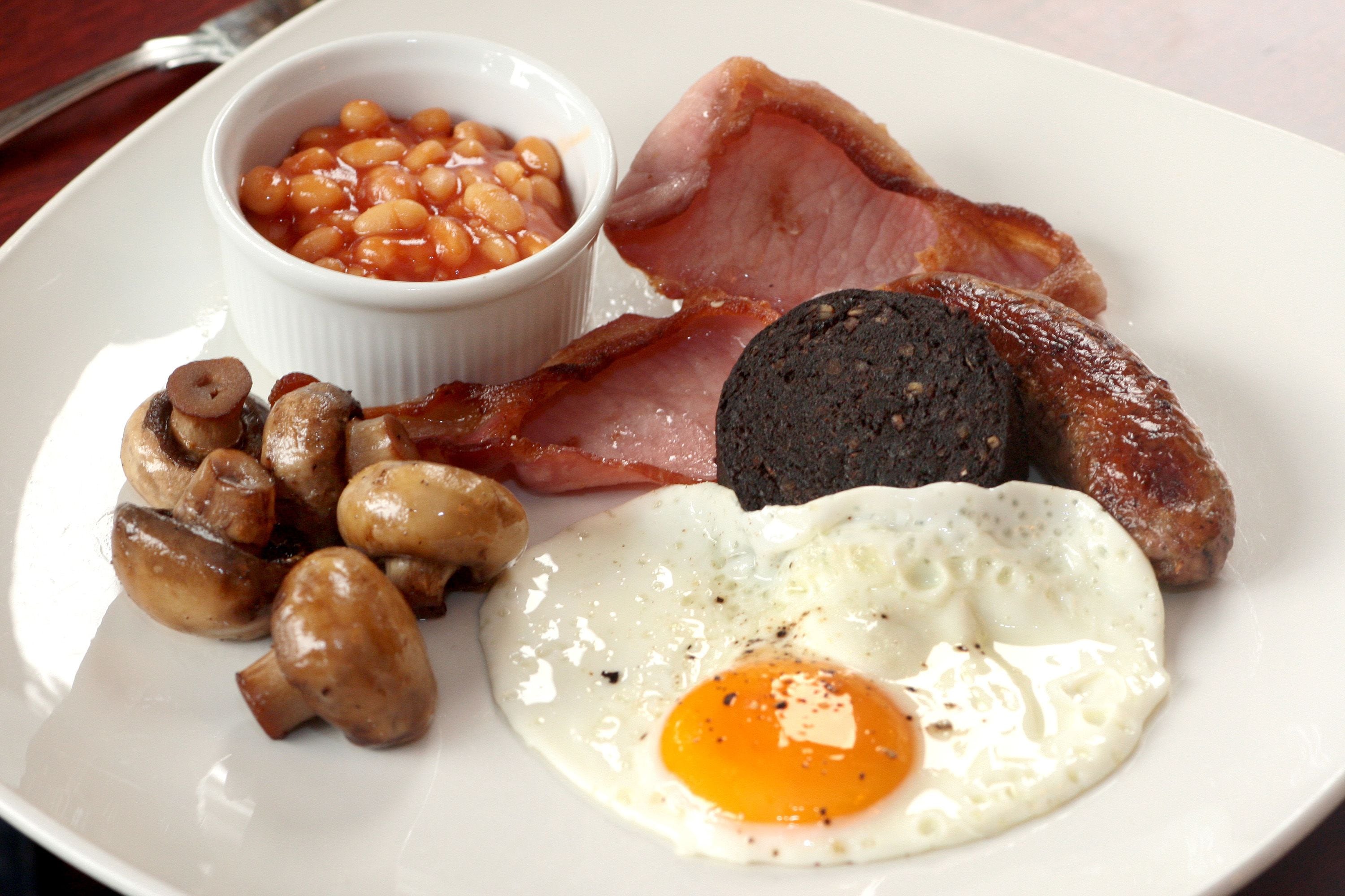 Une assiette de mets pour le petit-déjeuner comprenant du bacon, des œufs, des champignons, des haricots et une saucisse noire.