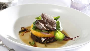 Un tazón blanco con un plato que contiene carne, verduras y un elemento amarillo, posiblemente una fruta o verdura.