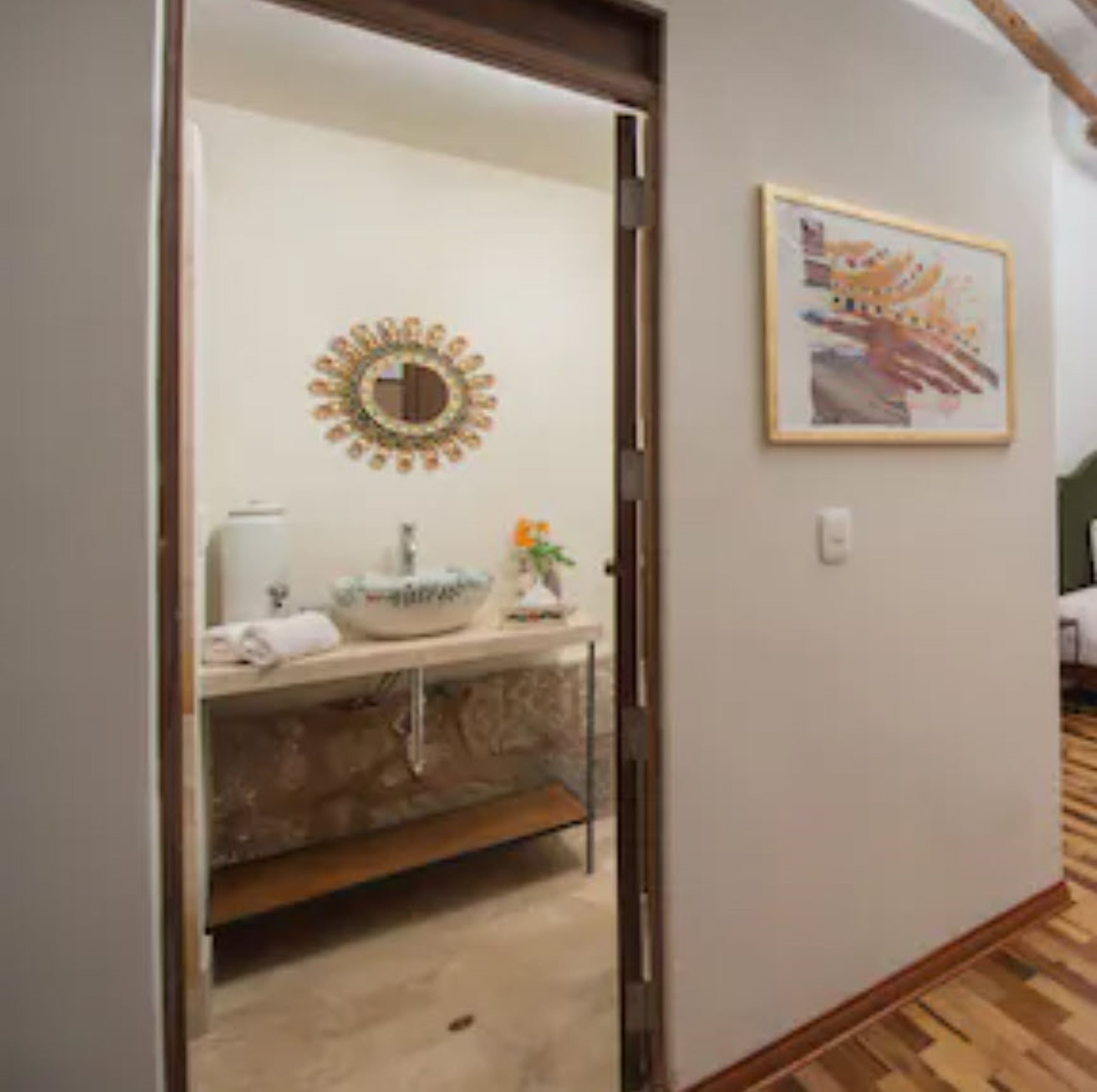 Een badkamer met een ronde spiegel, een wastafel en een kunstwerk in een lijst aan de muur.