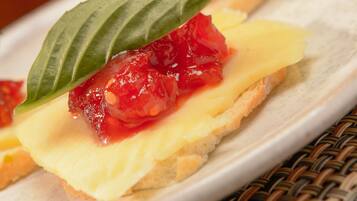 Un plato con un postre que incluye una porción de pastel coronada con dulce de fruta roja y una hoja de albahaca.