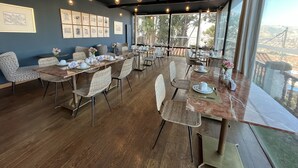 A dining area with tables set for tea service, framed artwork on the walls, and a view of a cityscape through large windows. - Palacio Manco Capac by Ananay Hotels (Cusco)