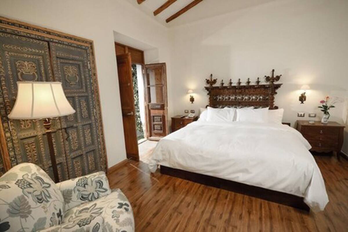 Un dormitorio con una cama grande, cabecera de madera, mesita de noche, lámpara y sofá estampado.