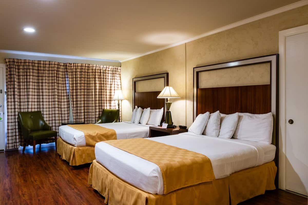 Una habitación de hotel con dos camas, una silla, una lámpara y una cortina a cuadros.
