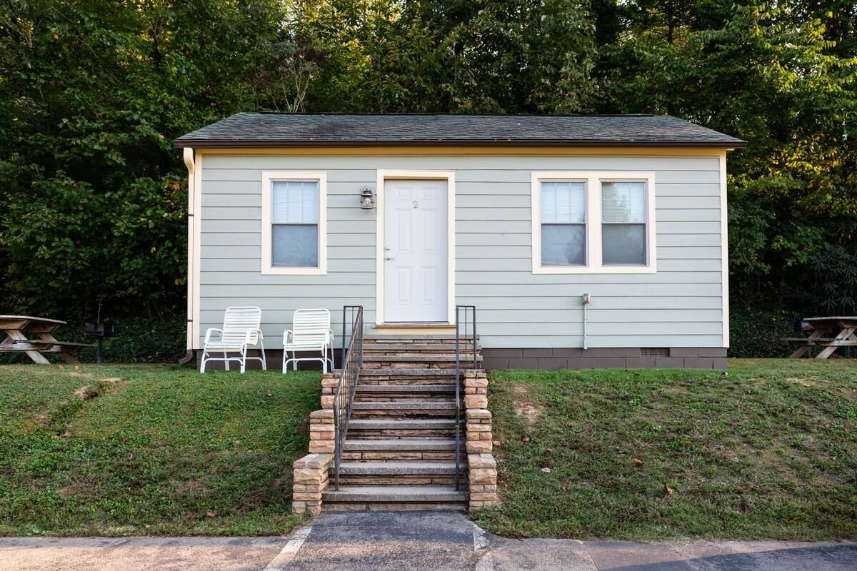 Una casa pequeña de un solo piso, con una puerta principal, dos ventanas y un conjunto de escalones de piedra que conducen a la entrada.