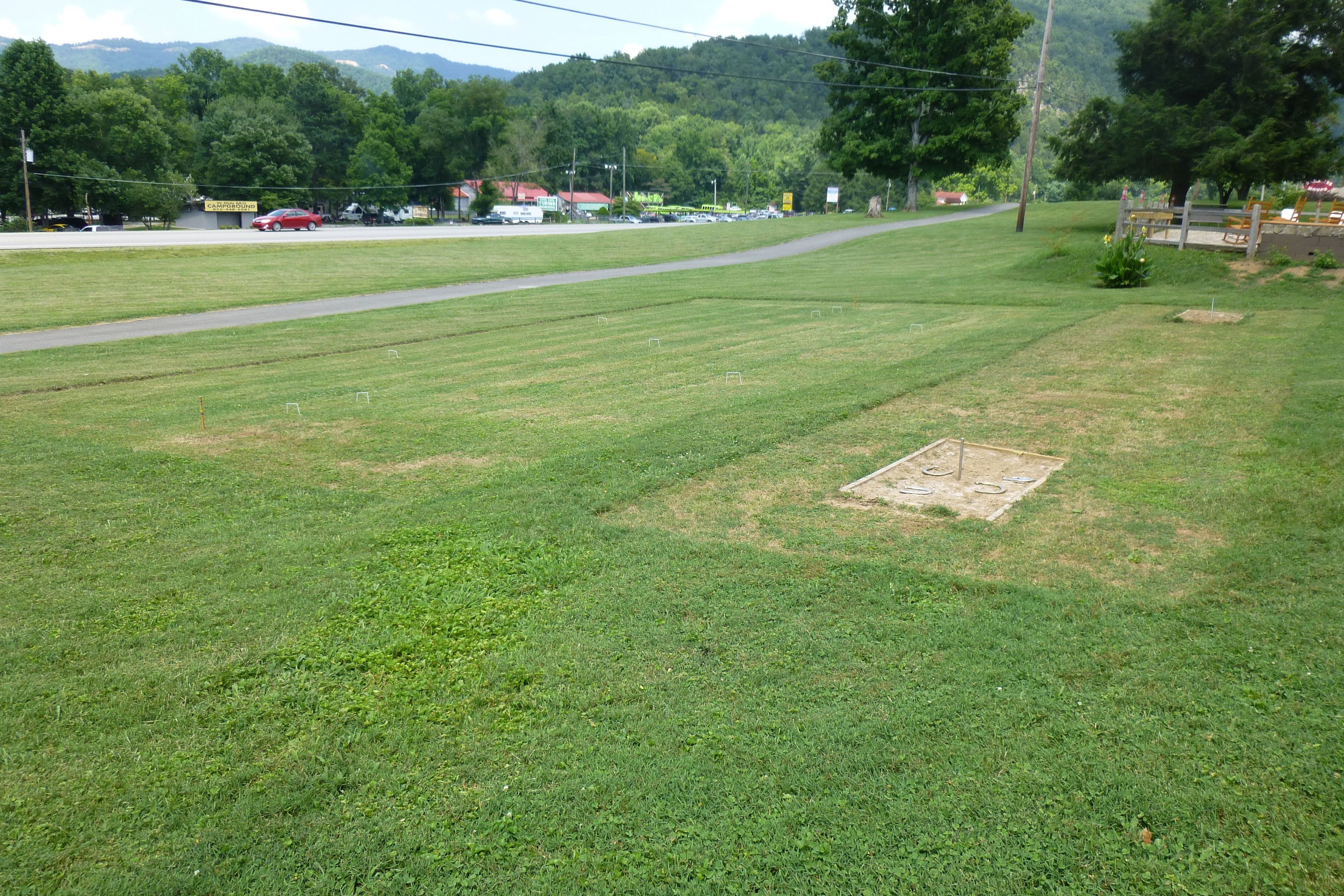 A grassy field with a baseball diamond and a road in the background.