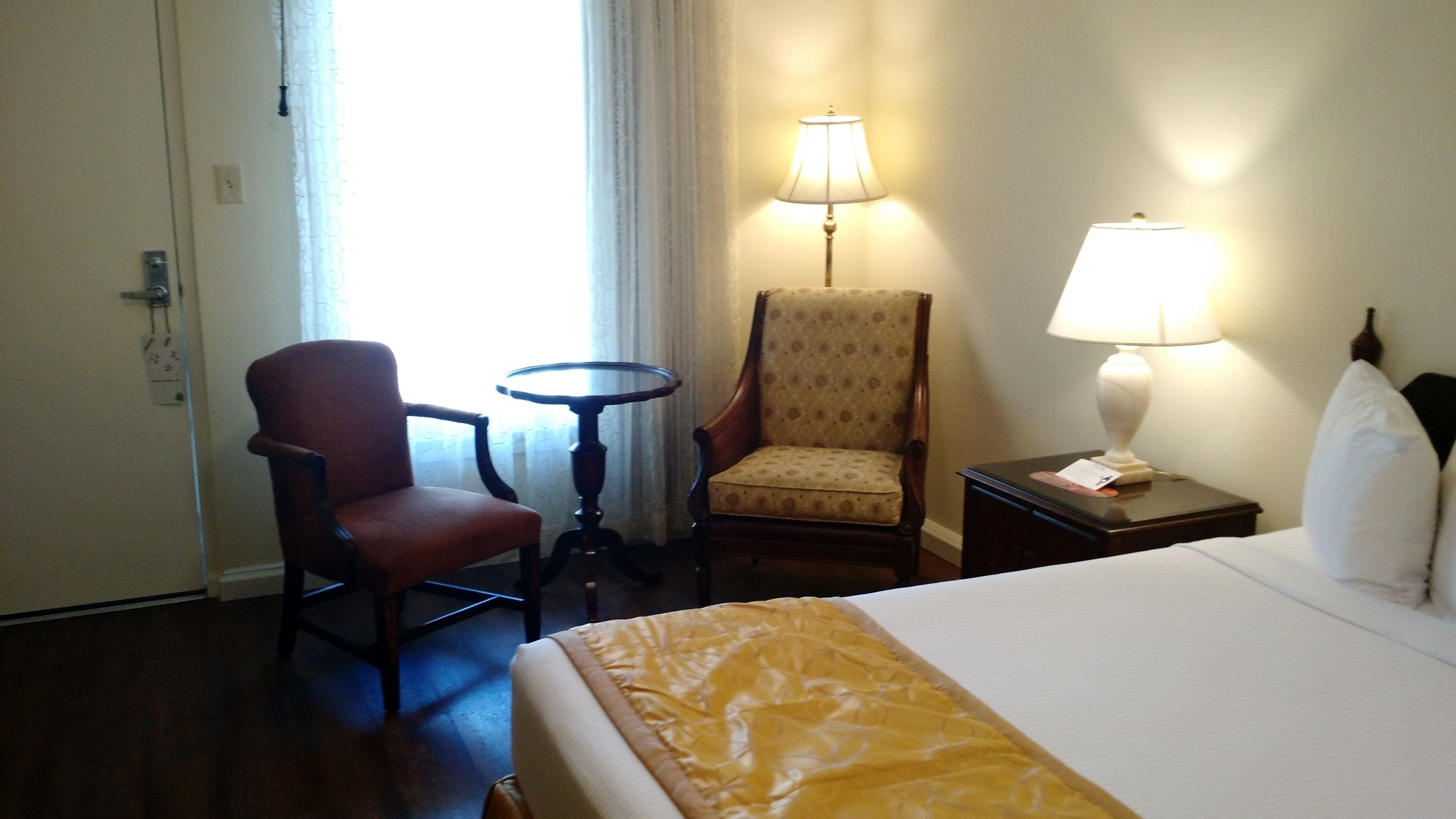 Habitación de hotel con cama, dos sillas, una mesita y dos lámparas de noche.