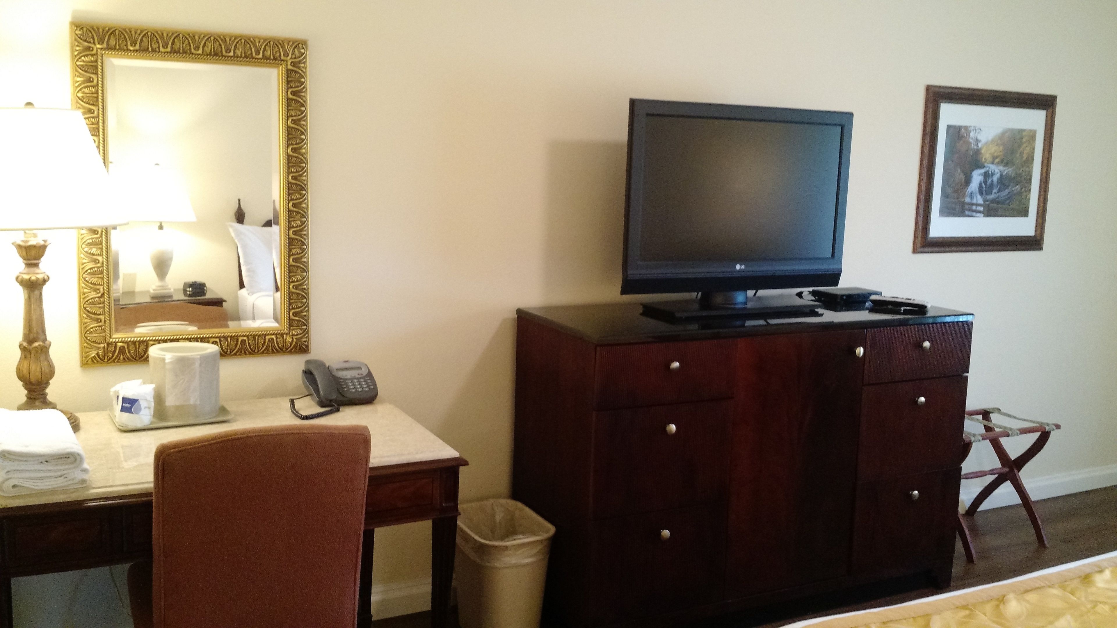 Ein Hotelzimmer mit Schreibtisch, Fernseher, Telefon, Papierkorb und Stuhl.