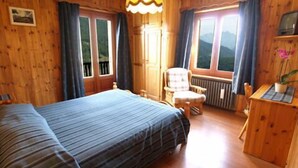 Una habitación de madera con una cama, una silla, un escritorio y una ventana con cortinas.