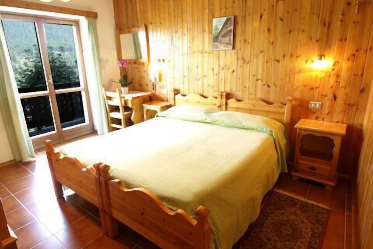 A wooden-paneled bedroom with a bed, bedside tables, a desk, and a chair.