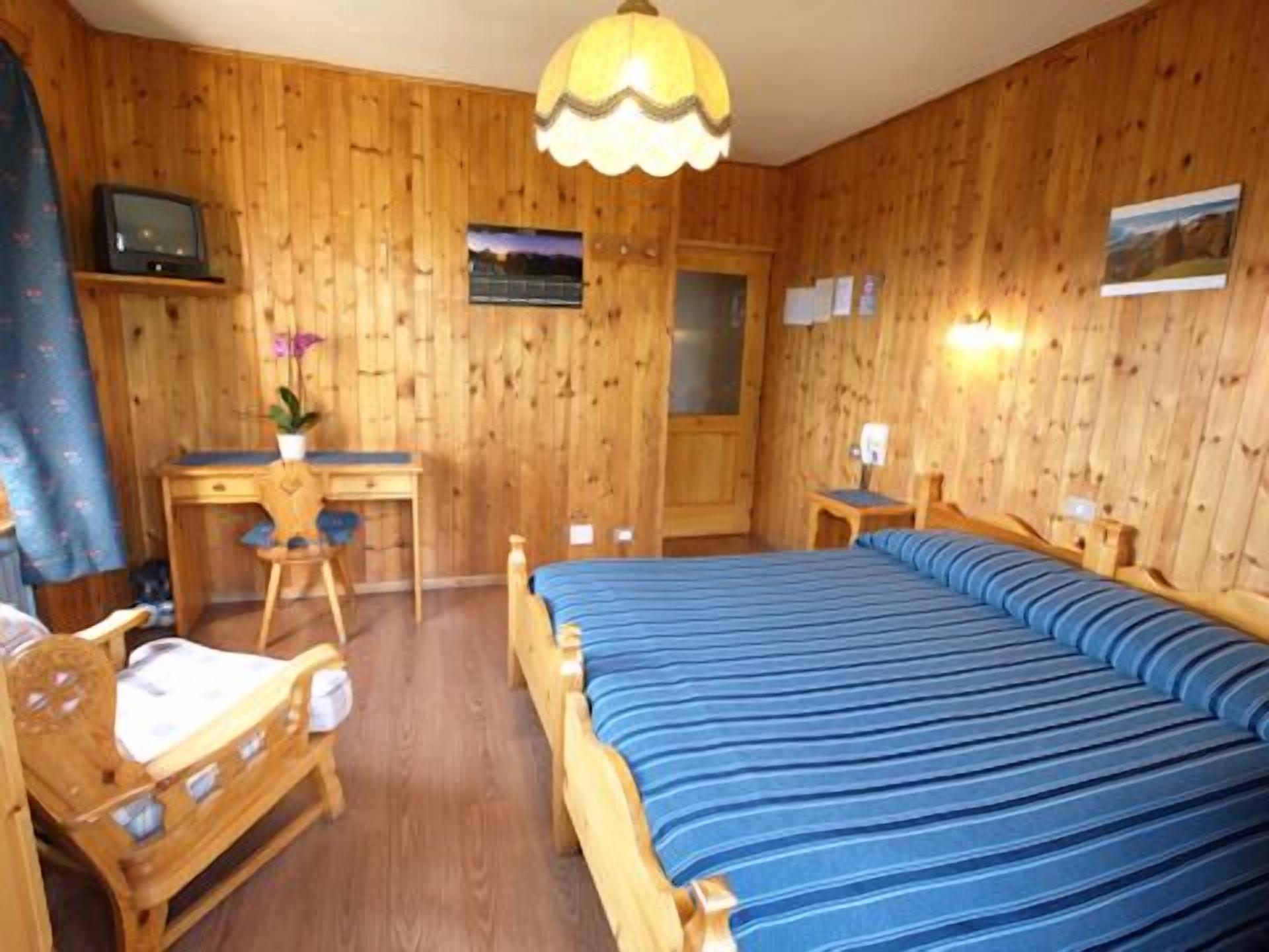 A wooden-paneled room with a bed, desk, chair, and a small table.