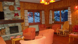 Una habitación acogedora con muebles de mimbre, una chimenea de piedra y amplios ventanales con vistas nevadas.