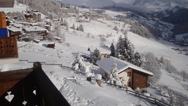 Un pueblo cubierto de nieve con casas tradicionales de madera, una valla de madera y montañas al fondo.