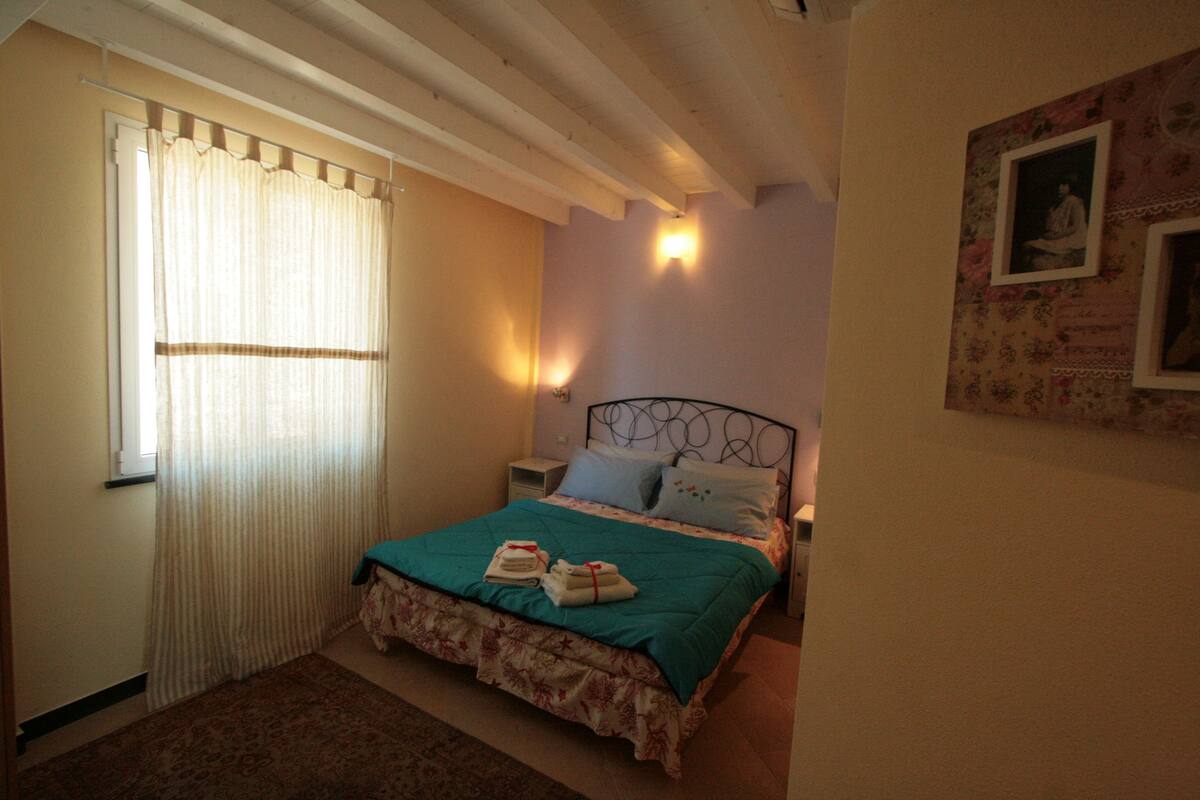 A bedroom with a bed, a nightstand, a wall-mounted lamp, and a window with curtains.
