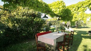 Un área de comedor al aire libre con mesa y sillas, rodeada de exuberante vegetación y árboles.