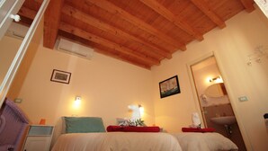 Habitación de hotel con dos camas, vigas de techo de madera, baño con lavabo y espejo, y un escritorio pequeño con lámpara.