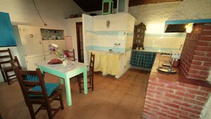 Cocina compacta con horno de ladrillo, zona de comedor con mesa y sillas, y un mueble pequeño con vajilla.