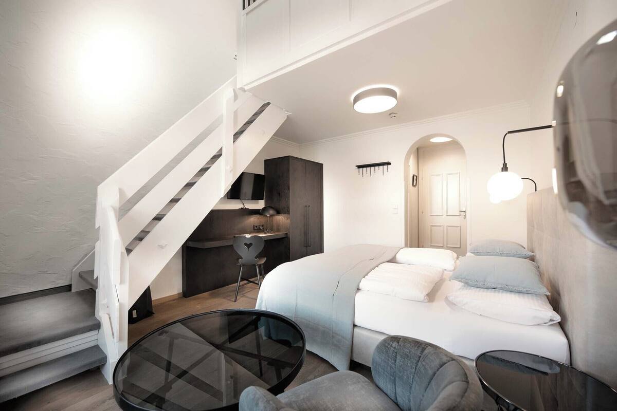 A modern interior with a staircase, a dining area, a bed, and a seating area.