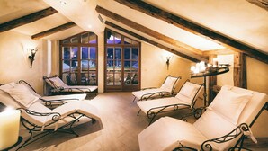 A cozy attic bedroom with four reclining chairs, a small table with candles, and a large window offering a view of the outdoors. - Berg-Leben (Grossarl)