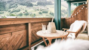 A wooden deck with a round table and two chairs, overlooking a green valley with houses. - Berg-Leben (Grossarl)